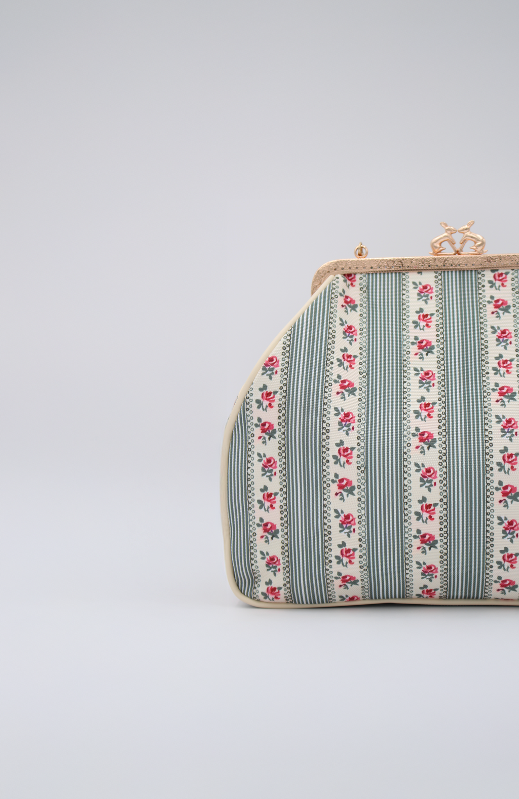 Herança, a vintage handbag with vertical green stripes, red floral patterns, and a gold clasp, is shown against a plain light background. Only the right side of this elegant bag is visible.